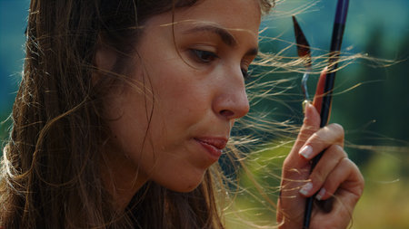 Portrait of creative painter biting lip working on picture in windy day. Talented artist holding...