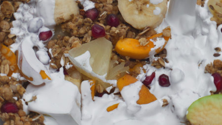 Natural yogurt pouring on sweet granola with pieces tasty fruits super slow motion close up. Baked...