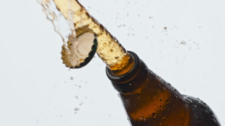 Cider splashing misted flask closeup. Drops trickle down beer bottle. Cold fresh lager beverage foaming fountaining at white background. Unfiltered alcohol carbonated liquor pouring out slow motionの写真素材
