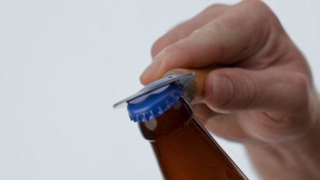 Fresh beer opening with bottle opener hold by unknown man at white background close up. Metal device...