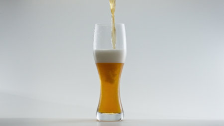 Fresh tasty lager beer filling clear glass in super slow motion close up. Stream of wheat alcohol drink pouring into transparent goblet at white background. Hop liquid bubbling foaming in mug.の写真素材