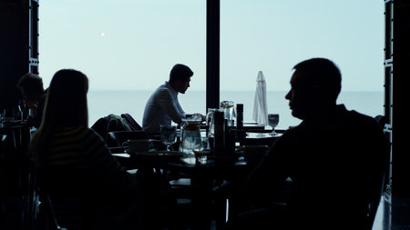 Restaurant visitor having dinner in stylish dark interior. Customer silhouettes resting evening...