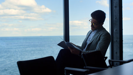 Businessman reading contract papers at sea view. Thinking manager analyzing data looking panorama window. Focused man lawyer checking finance documents corporate report. Male professional at work.の写真素材