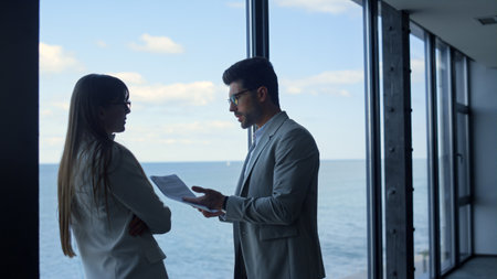 Boss discussing marketing report with stressed businesswoman at panorama window. Two business...