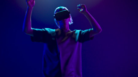 Millennial man partying with invisible 3D avatar. Virtual reality goggles person exciting playing neon background. VR-box youngster moving relaxing slow motion. Modern technological experience conceptの写真素材