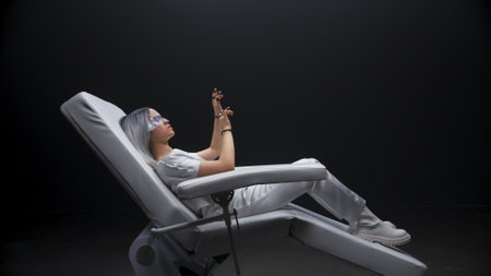 Involved gamer getting AI experience dark room. White hair haptic gloves woman sitting armchair. Future device student touching playing metaverse videogame slow motion. Nano technologies conceptの写真素材