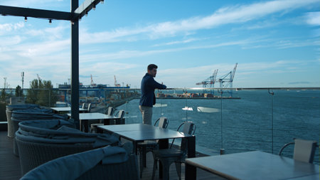 Young businessman resting outdoors enjoying sea view on glass cafe terrace. Handsome business owner...