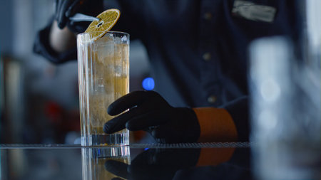 Bartender hands forceps putting lemon slice in glass closeup. Unknown barman adding ingredients at drink for party in restaurant. Unrecognizable person decorating cocktail for people conceptの写真素材
