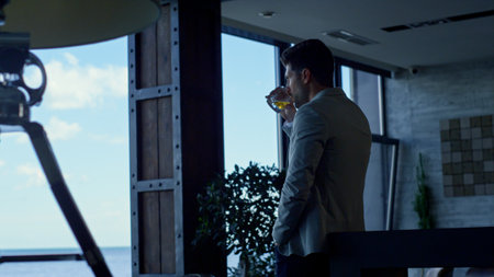 Businessman drinking whiskey in hotel lounge. Good looking gentleman tasting beverage in luxury conference hall. Leader person enjoying bourbon and relaxing. Successful man spending vacation conceptの写真素材