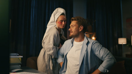 Embarrassed guy talking video call at home closeup. Bearded man hiding carefree wife behind back. Positive woman distracting husband from virtual chat. Smiling freelancer sitting remote workの写真素材