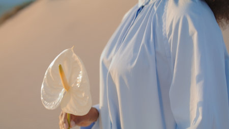 Attractive fashion model holding white flower at evening desert closeup. Relaxed calm african...