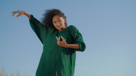 Graceful african american girl dancing at nature in front gray summer sky close up. Curly attractive woman dancing sensually in black dress. Inspired brunette moving hands smoothly looking camera.の写真素材