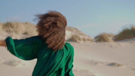 Contemporary dancer performing at sand desert windy summer day close up. Young african american woman dancing at dunes wearing black dress. Curly girl brunette moving sensually on beautiful nature.の写真素材