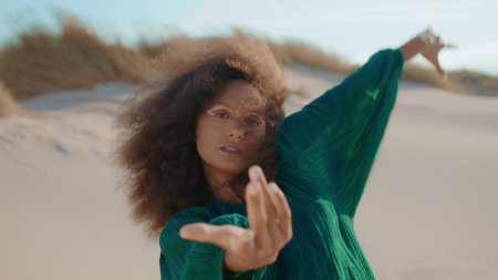 Flexible african american woman dancing improvisation on sand dunes closeup. Curly young brunette...