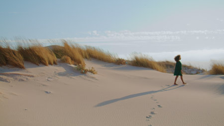 Unknown young girl walking summer desert leaving footprints on sand. Silhouette of african american...