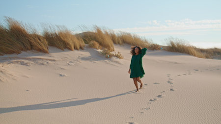 African american girl jogging down sand hill leaving footprints at summer desert. Attractive relaxed woman walking on dunes wearing black dress. Young brunette enjoy holiday at wilderness nature.の写真素材