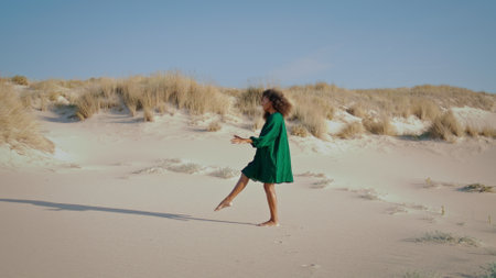 Young flexible woman dancing modern dance at desert dunes in black dress. Curly brunette dancer performing on sand wilderness summer day. African american pretty girl making smooth body movements.の写真素材
