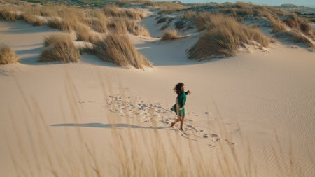 African american woman dancer performing freestyle at summer desert in distance. Curly brunette girl making graceful movements on sand dunes with dry grass. Inspired lady dancing in black dress.の写真素材