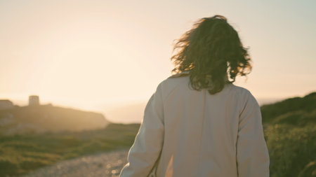 Happy girl going sunset seashore rear view. Cheerful woman rejoicing in sunlight enjoying wonderful life at ocean mountain evening. Curly satisfied silhouette walking spinning chill in quiet place.の写真素材