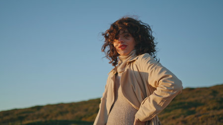 Casual girl posing evening sunlight at seaside. Pretty smiling woman touch hair enjoying sunset at...