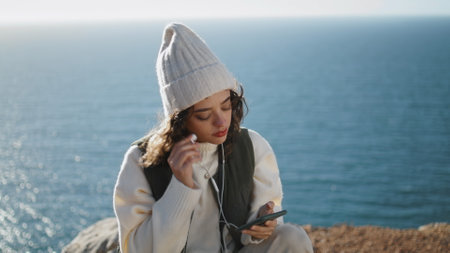 Pretty girl turn player at calm ocean closeup. Serene tourist enjoying music in earphones closing eyes. Happy beautiful woman listening to favorite song relaxing on sea mountain. Peaceful mood leisureの写真素材