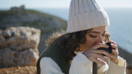 Adventure woman drink coffee on ocean cliff picnic closeup. Serene morning time. Thinking traveler enjoying warm beverage admire view on spring weekend. Pretty curly girl looking camera relax outdoorsの写真素材