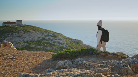 Hiking girl talking phone at calm ocean sunset. Excited tourist walking mountain with backpack using smartphone. Adventure woman enjoy active vacation trekking sea cliff. Roaming communication conceptの写真素材