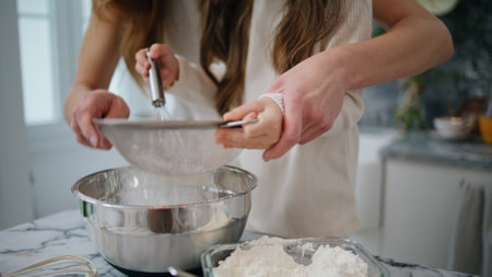 Mother daughter hands cooking dough at home close up. Unrecognizable family preparing pastry together at kitchen. Unknown helping woman holding child girl arms sifting flour. Baby making food with momの写真素材