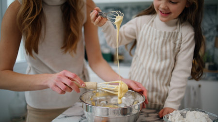 Mother daughter hands creating dough at home close up. Positive family preparing pastry together at kitchen. Smiling woman mixing whisk spending time with child. Mommy teaching lovely kid to cookの写真素材