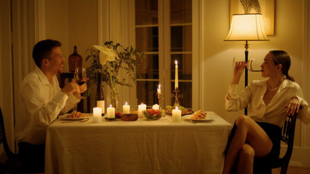 Laughing newlyweds drinking wine glasses at home closeup. Smiling man gesturing woman talking emotionally at romantic date interior. Cheerful lovers having fun at candles served table togetherの写真素材