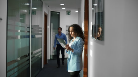 Closeup positive partners working tablet computer hallway. Laughing professionals discussing plan together at business center. Successful team analyzing communicating in corridor. Man approaches womanの写真素材