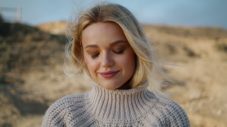 Autumn model enjoying windy weather. Thoughtful woman posing picturesque nature in wild wheat field. Blonde girl straightens hair resting valley alone. Breeze blows lightly playing with lady hairstyleの写真素材