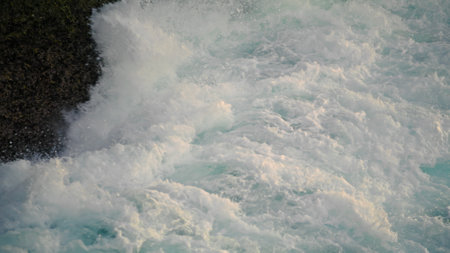 Sea splashes breaking by hill outside closeup. White spray crashing by huge rocks in shallows. Large ocean waves washing dark mountain at dusk nature. Scenic stormy water streams landscape conceptの写真素材