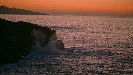 Dark cliff at ocean sunrise morning. Tranquil sea shore calm waves at orange picturesque sunset dusk. Mountain hill silhouette at beach coastline with golden skyline. Travelling tourism conceptの写真素材