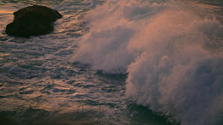 Splashing waves covering rock at sunset closeup. Cold sea water foaming at evening shore. Swirling...