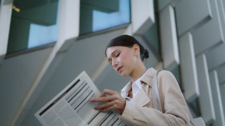 Young attractive woman turning newspaper pages standing alone outdoors close up. Confident businesswoman reading tabloid publication in news paper. Smart successful manager searching information.の写真素材