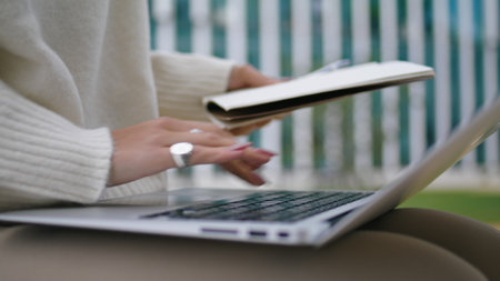 Woman hands typing laptop outdoors holding paper copybook close up. Unknown girl freelance worker working remotely using wireless computer. Lady fingers with beautiful rings pressing notebook keyboardの写真素材