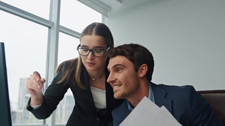 Happy team working computer in office closeup. Joyful manager throwing papers celebrating successful company results with beautiful colleague. Two employees checking data finishing marketing project.の写真素材
