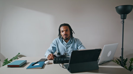 Positive arranger posing camera home zoom on. Handsome sound producer relaxing in apartment remotely alone portrait. Smiling african american man sitting table looking attentively after work closeupの写真素材