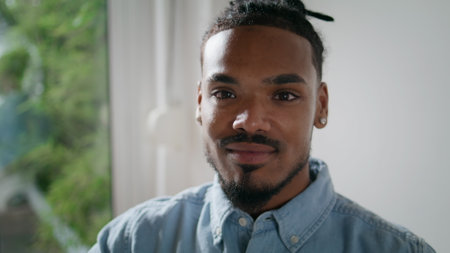 Smiling man posing camera home alone closeup. African american student looking attentively in studio...