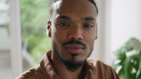 Positive man posing camera home alone closeup. African american student looking attentively in studio portrait. Black hair contemporary freelancer face working indoors. Human appearance conceptの写真素材