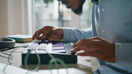 Man arms using keyboard home closeup. Anonymous african american dj touching console controllers. Bearded student looking attentively typing brown skin fingers. Unrecognizable guy creating musicの写真素材