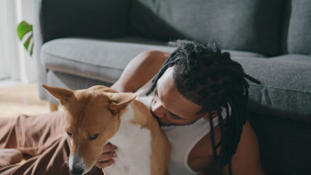 Friendly guy cuddling pet at living room closeup. Young man stroking puppy with pleasure good emotions. African american teenager scratching adorable dog laying at floor. Animals and owners conceptの写真素材