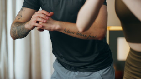 Fit man training squats with slim woman at home close up. Young attractive couple making fitness exercise for strong legs together. Active sporty family workouting in apartment wearing sportswear.の写真素材