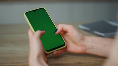 View of woman hands with green screen smartphone close up. Unknown young girl holding chroma key phone watching social media touching swiping touchscreen. Lady browsing Internet video content blogs.の写真素材