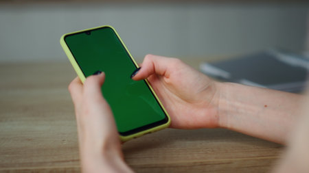 Unknown woman holding greenscreen smartphone scrolling touchscreen at home close up. Young girl using chroma key mobile phone to watching social network surfing in internet. Technology concept.の写真素材