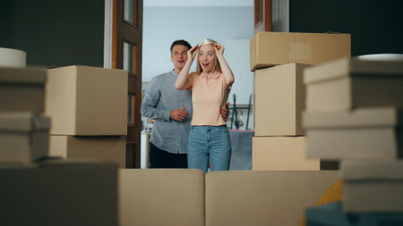Excited newlyweds hugging moving at new apartment full of packed carton boxes. Young attractive woman surprising entering in modern living room. Cheerful family enjoy relocation in mortgage house.の写真素材