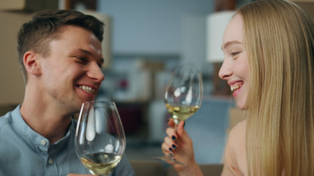 Young family celebrating relocation drinking wine clinking glasses close up. Lovely happy couple sitting in new house living room near carton boxes enjoying own apartment. Housewarming party together.の写真素材