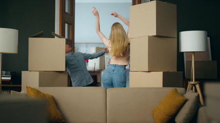 New cheerful homeowners funny dancing between carton packed boxes celebrating buying own property. Young positive family fooling together happy about moving in new apartment. Relocation concept.の写真素材