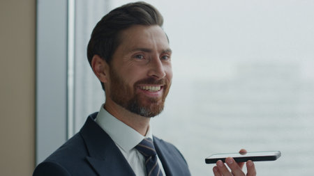 Smiling attractive manager finishing telephone talk satisfied by success working negotiation close up. Happy bearded business man holding modern smartphone using gadget for professional communicating.の写真素材